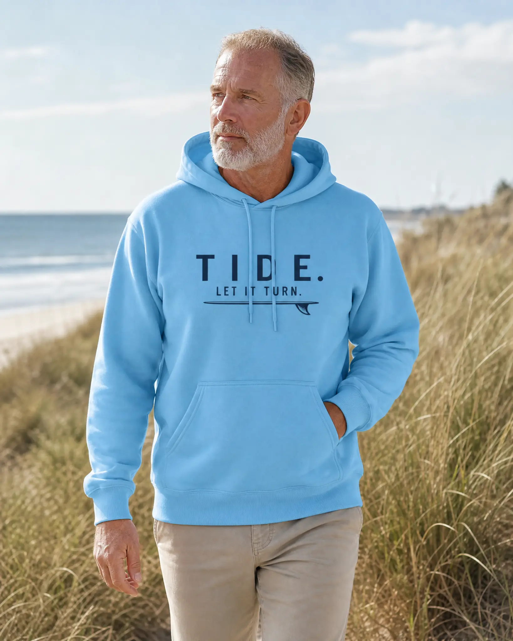 Man wearing the Tide Let It Turn sky-blue hoodie near the beach